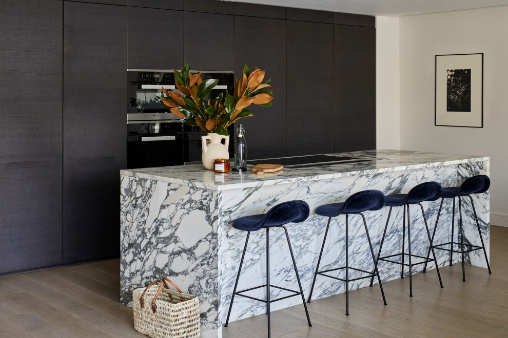 Photo of a contemporary kitchen in London with flat-panel cabinets, dark wood cabinets, marble benchtops, light hardwood floors and with island.