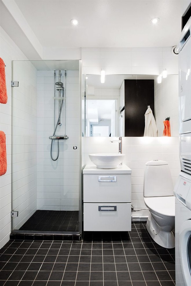 Photo of a mid-sized scandinavian 3/4 bathroom in Stockholm with flat-panel cabinets, white cabinets, a corner shower, a two-piece toilet, black tile, white tile, white walls, a vessel sink, porcelain tile, ceramic floors and a hinged shower door.
