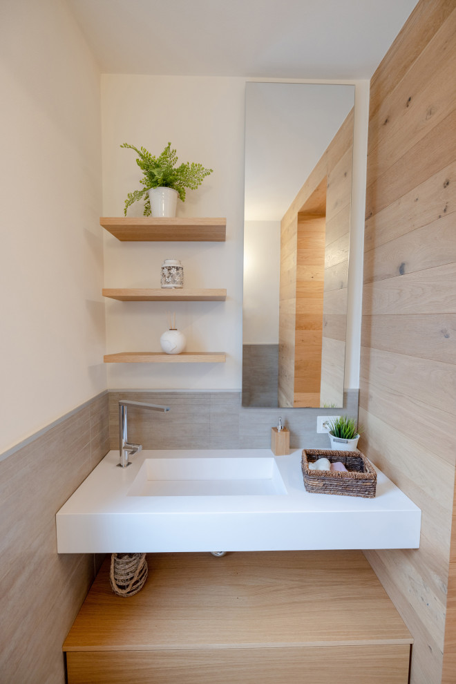This is an example of a small contemporary cloakroom in Milan with flat-panel cabinets, light wood cabinets, a two-piece toilet, grey tiles, porcelain tiles, brown walls, medium hardwood flooring, an integrated sink, engineered stone worktops, grey floors, white worktops, a floating vanity unit and wood walls.
