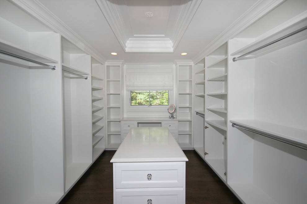 This is an example of a large transitional gender-neutral walk-in wardrobe in New York with open cabinets, dark hardwood floors and white cabinets.