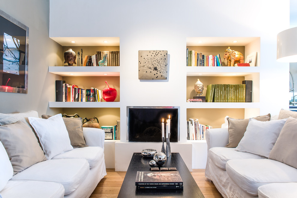 This is an example of an eclectic living room in Other with a library, white walls, light hardwood floors, a ribbon fireplace and a metal fireplace surround.