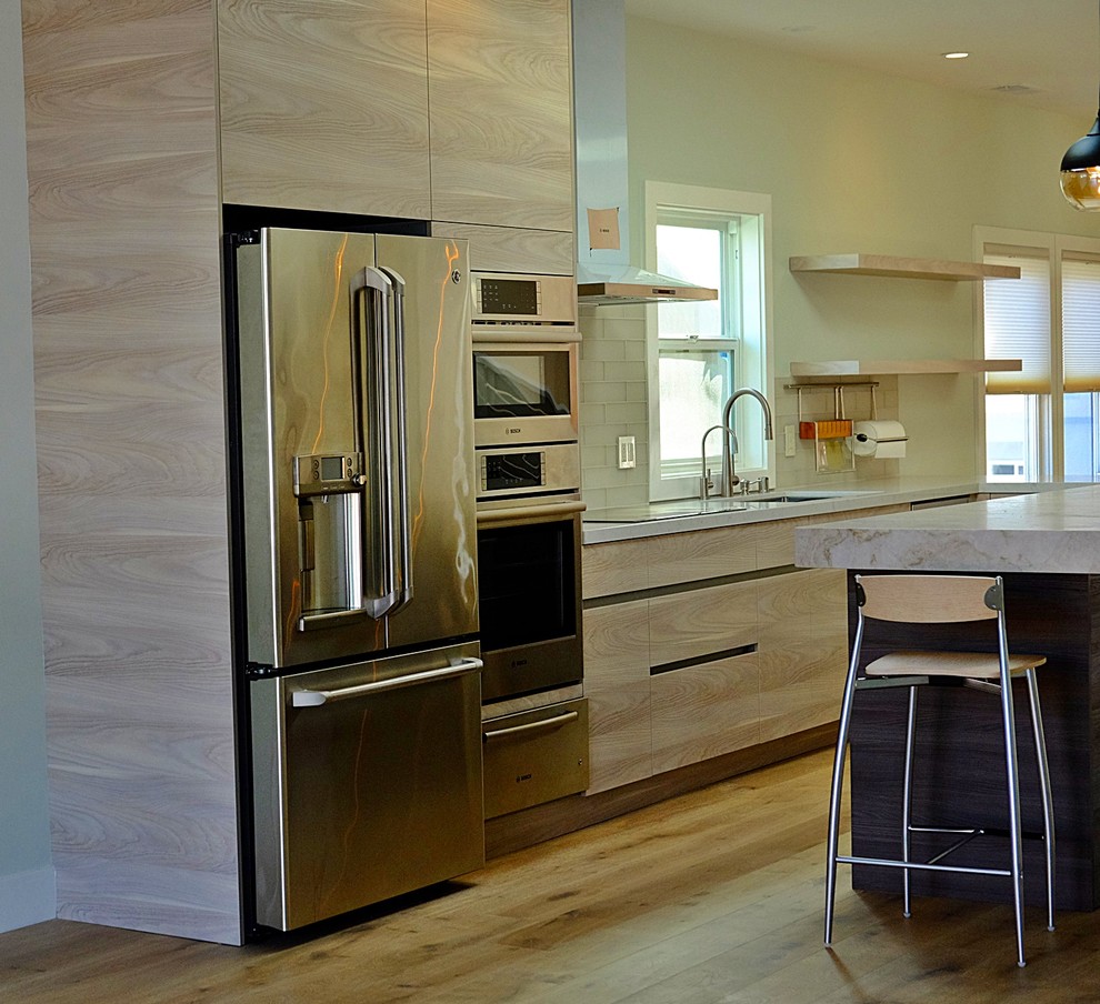 Photo of a mid-sized contemporary l-shaped open plan kitchen in San Francisco with an undermount sink, flat-panel cabinets, light wood cabinets, quartz benchtops, white splashback, glass tile splashback, stainless steel appliances, light hardwood floors and with island.