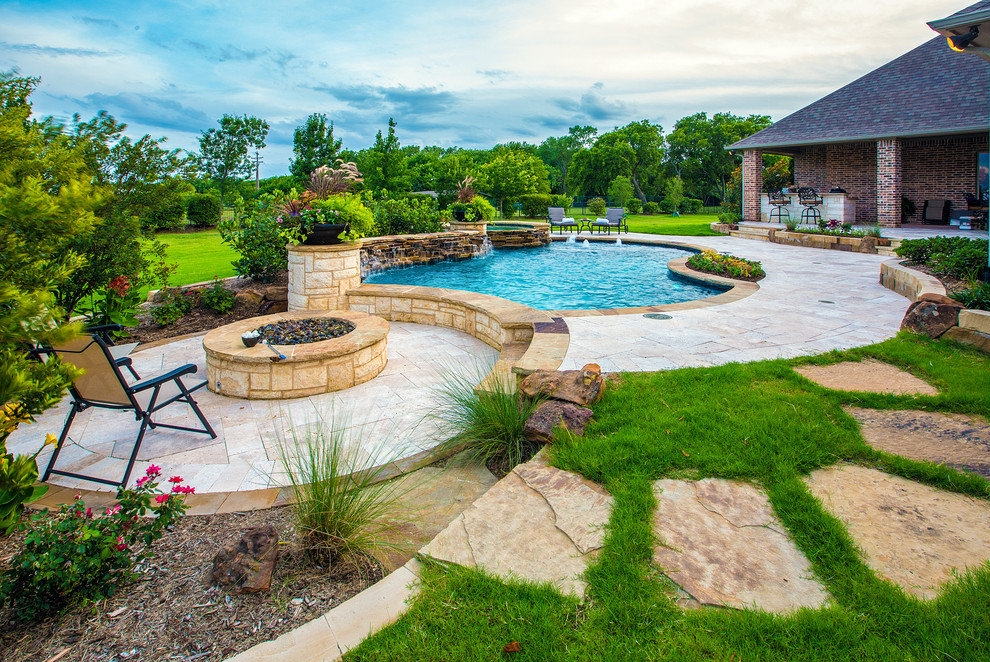 This is an example of a mid-sized traditional backyard custom-shaped natural pool in Dallas with natural stone pavers and a hot tub.