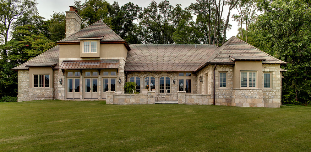 This is an example of an expansive two-storey beige house exterior in Other with stone veneer and a shingle roof.