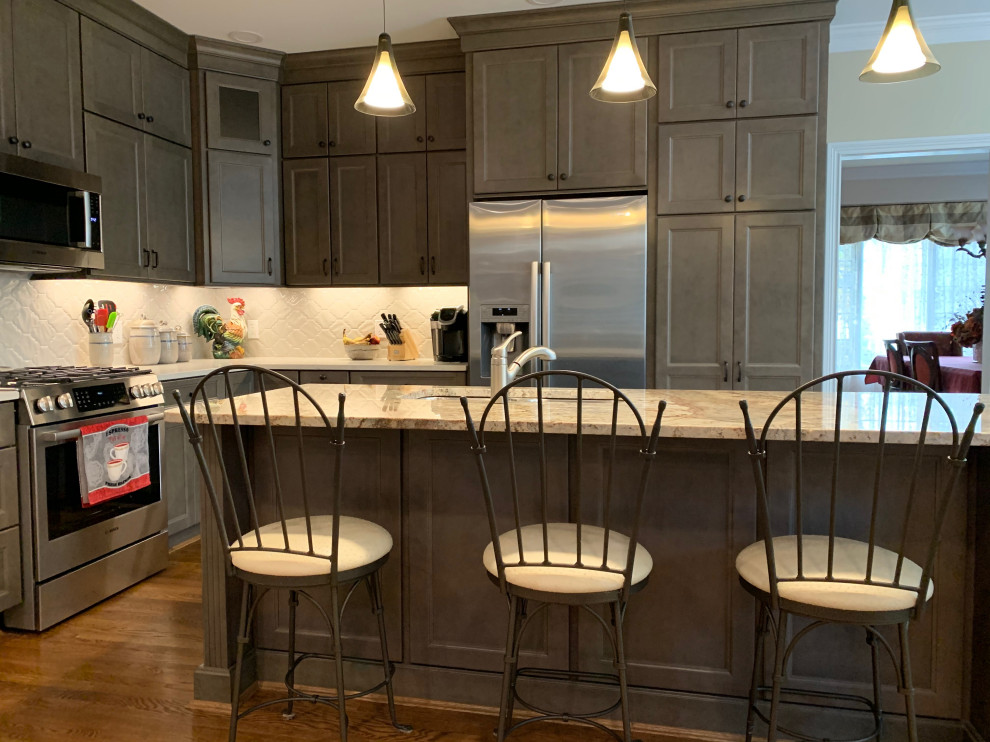 Inspiration for a mid-sized transitional l-shaped medium tone wood floor and brown floor eat-in kitchen remodel in Cincinnati with an undermount sink, recessed-panel cabinets, gray cabinets, quartz countertops, white backsplash, porcelain backsplash, stainless steel appliances, an island and white countertops