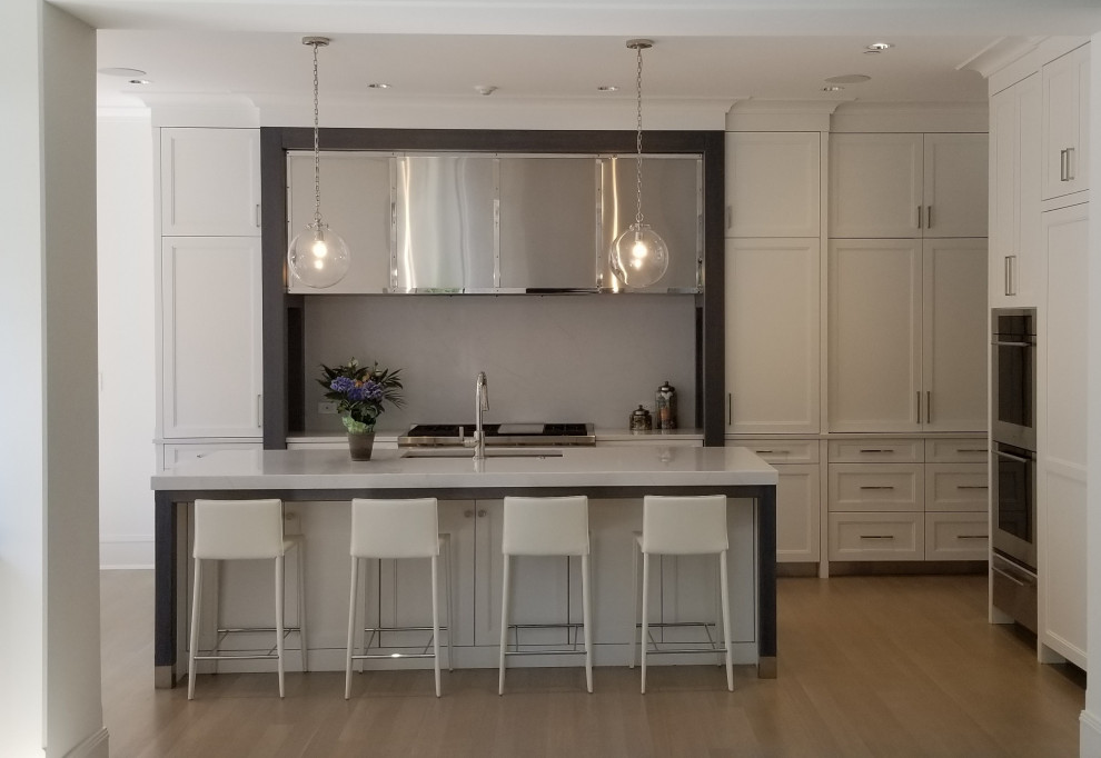 Example of a mid-sized transitional l-shaped light wood floor eat-in kitchen design in Chicago with recessed-panel cabinets, white cabinets, quartz countertops and an island