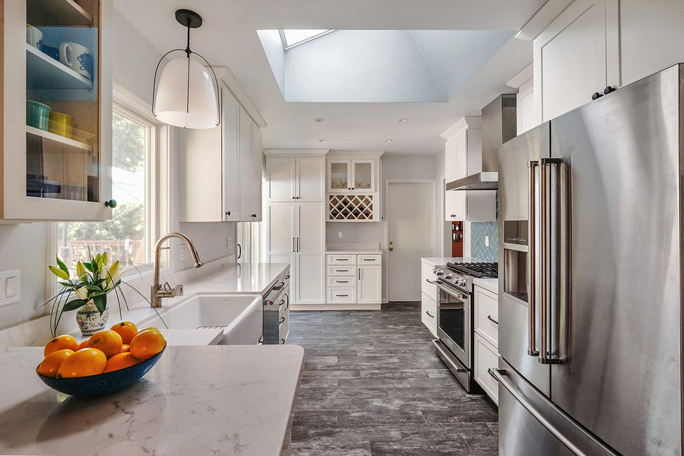 Inspiration for a transitional galley kitchen in San Francisco with a farmhouse sink, recessed-panel cabinets, white cabinets, blue splashback, subway tile splashback, stainless steel appliances, grey floor and beige benchtop.