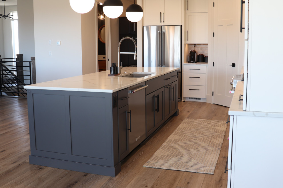 Example of a large transitional l-shaped medium tone wood floor and brown floor open concept kitchen design with a single-bowl sink, shaker cabinets, white cabinets, quartz countertops, gray backsplash, subway tile backsplash, stainless steel appliances, an island and white countertops