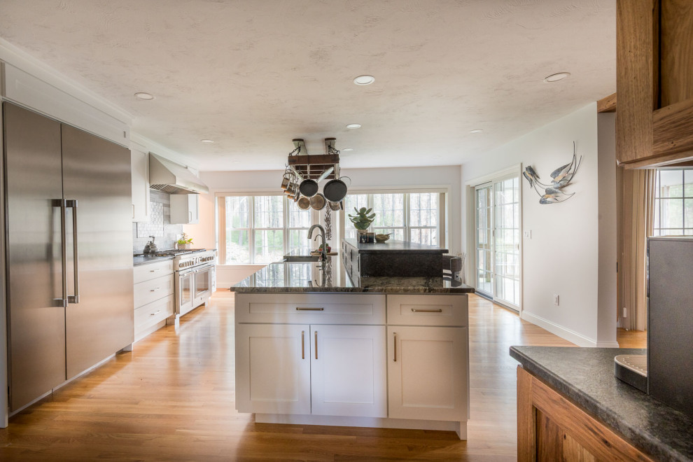 Inspiration for a large transitional single-wall light wood floor and brown floor eat-in kitchen remodel in Boston with a farmhouse sink, shaker cabinets, white cabinets, granite countertops, gray backsplash, ceramic backsplash, stainless steel appliances, an island and gray countertops