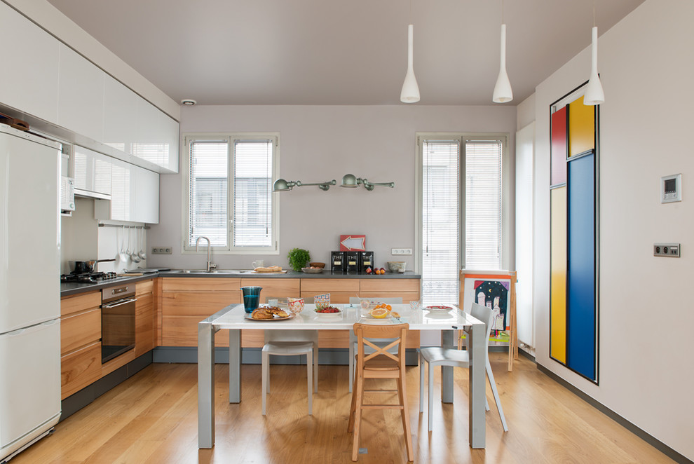 This is an example of a large contemporary l-shaped eat-in kitchen in Paris with flat-panel cabinets, light wood cabinets, white appliances, light hardwood floors and no island.