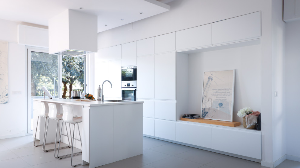 Inspiration for a large contemporary single-wall open plan kitchen in Rome with a drop-in sink, flat-panel cabinets, white cabinets, laminate benchtops, stainless steel appliances, porcelain floors, with island, grey floor, white benchtop and recessed.