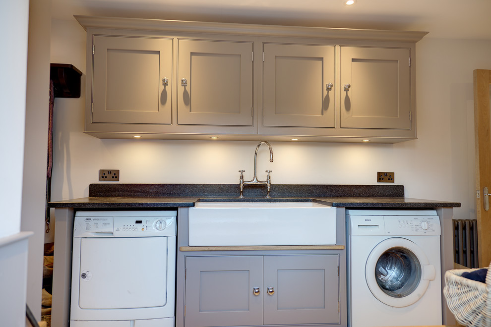 Inspiration for a mid-sized traditional galley laundry room in Hampshire with a farmhouse sink, flat-panel cabinets, grey cabinets, granite benchtops, limestone floors and a side-by-side washer and dryer.