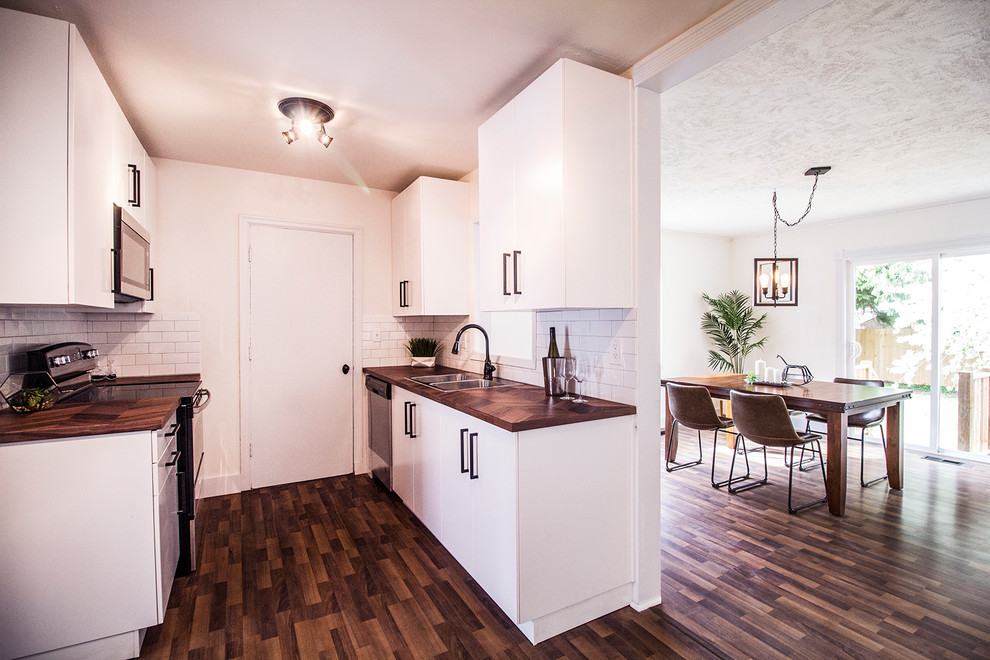 Small modern galley separate kitchen in Portland with a double-bowl sink, flat-panel cabinets, white cabinets, wood benchtops, white splashback, subway tile splashback, stainless steel appliances, dark hardwood floors, no island, brown floor and brown benchtop.