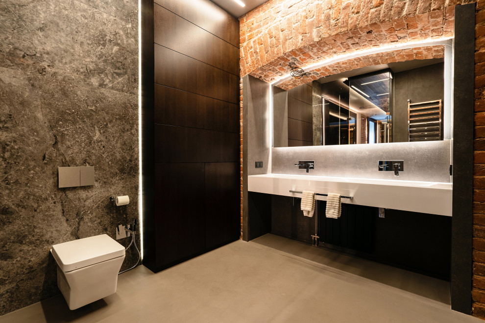 Inspiration for a large urban ensuite wet room bathroom in Saint Petersburg with flat-panel cabinets, white cabinets, a wall mounted toilet, grey tiles, marble tiles, concrete flooring, a submerged sink, solid surface worktops, grey floors, a sliding door, white worktops, an enclosed toilet, double sinks, a built in vanity unit and brick walls.
