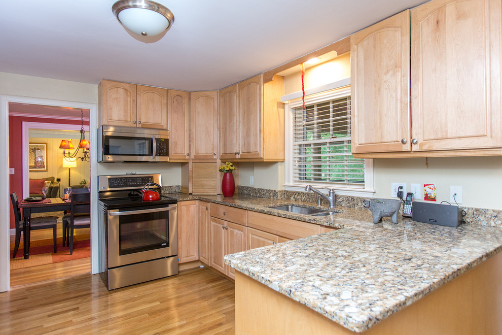 This is an example of a traditional kitchen in Boston with a drop-in sink, raised-panel cabinets, light wood cabinets, granite benchtops, stainless steel appliances and light hardwood floors.
