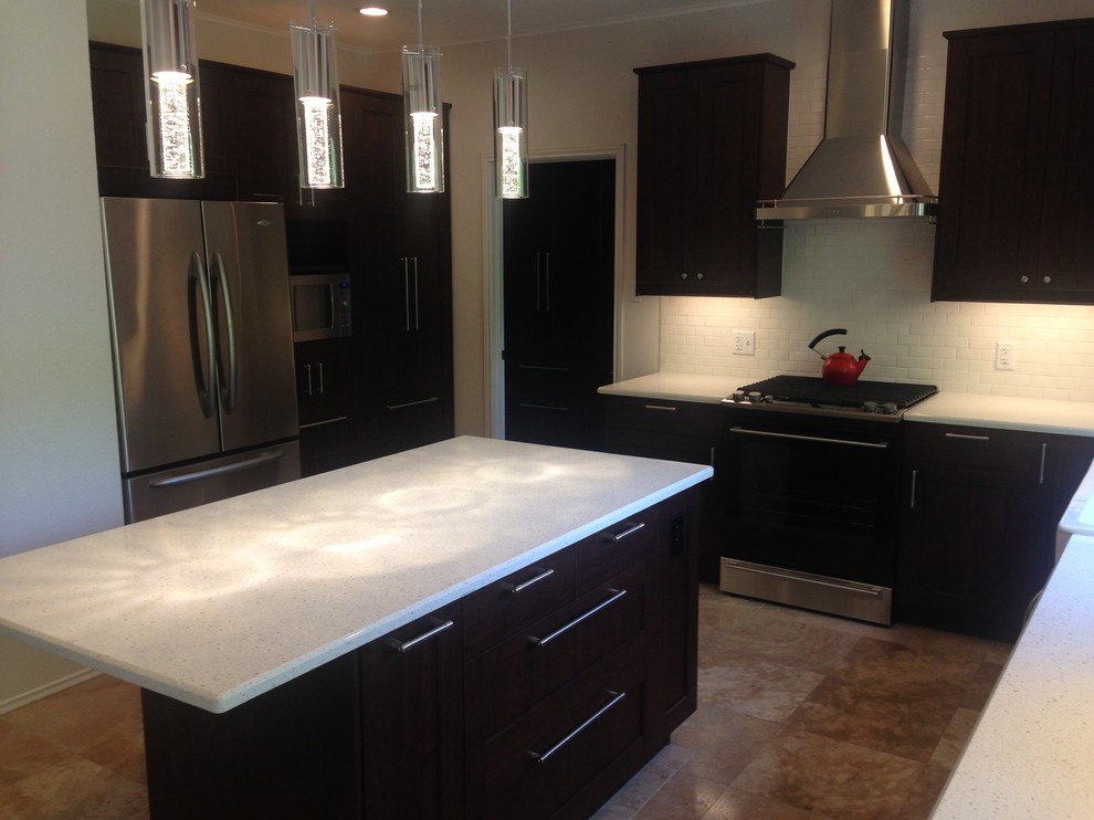 Enclosed kitchen - large transitional u-shaped porcelain tile and brown floor enclosed kitchen idea in Austin with a farmhouse sink, recessed-panel cabinets, dark wood cabinets, limestone countertops, white backsplash, subway tile backsplash, stainless steel appliances, an island and white countertops
