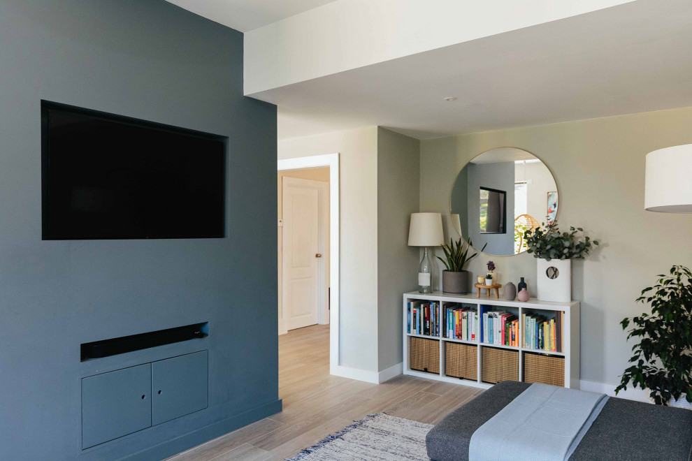 Modelo de salón abierto nórdico de tamaño medio con paredes grises, suelo de madera clara, estufa de leña, televisor colgado en la pared y suelo gris