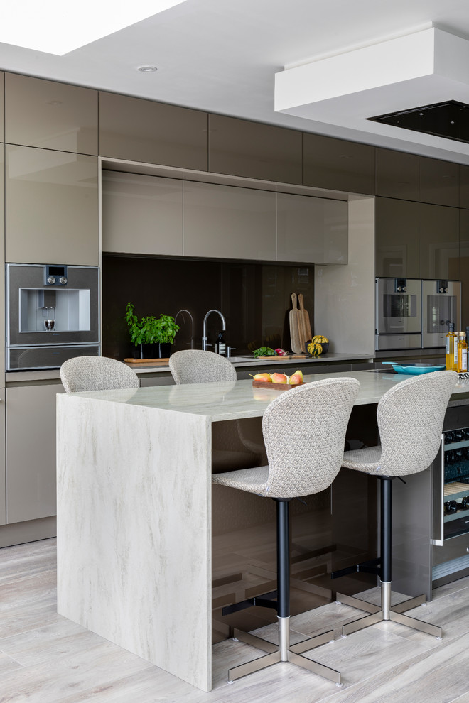 Design ideas for a large contemporary galley open plan kitchen in Surrey with a drop-in sink, flat-panel cabinets, grey cabinets, solid surface benchtops, metallic splashback, glass sheet splashback, stainless steel appliances, porcelain floors, with island, multi-coloured floor and beige benchtop.