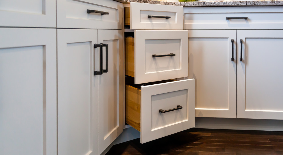 Large transitional u-shaped dark wood floor and brown floor kitchen photo in Calgary with an undermount sink, shaker cabinets, white cabinets, granite countertops, white backsplash, subway tile backsplash, stainless steel appliances and an island