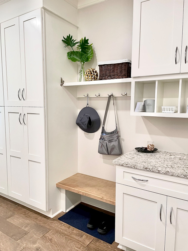 Photo of a mid-sized transitional single-wall utility room in Other with flat-panel cabinets, white cabinets, quartz benchtops, beige walls, medium hardwood floors, a concealed washer and dryer and grey benchtop.