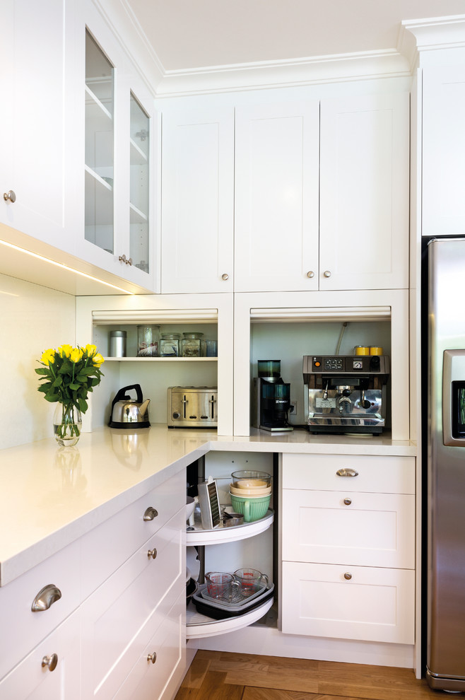 This is an example of a transitional kitchen in Melbourne with shaker cabinets, white cabinets, stainless steel appliances, white splashback, glass sheet splashback, medium hardwood floors and white benchtop.