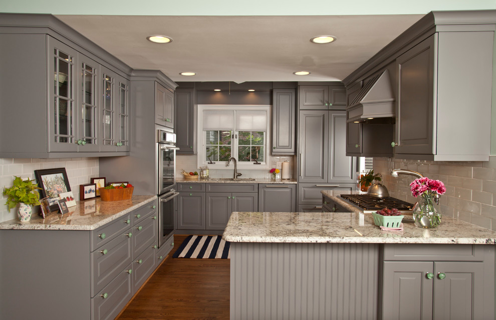 Photo of a traditional kitchen in Raleigh with raised-panel cabinets, grey cabinets, grey splashback, subway tile splashback, panelled appliances, dark hardwood floors, a peninsula and granite benchtops.