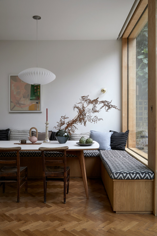 Photo of a large midcentury dining room in London with banquette seating, white walls and medium hardwood flooring.