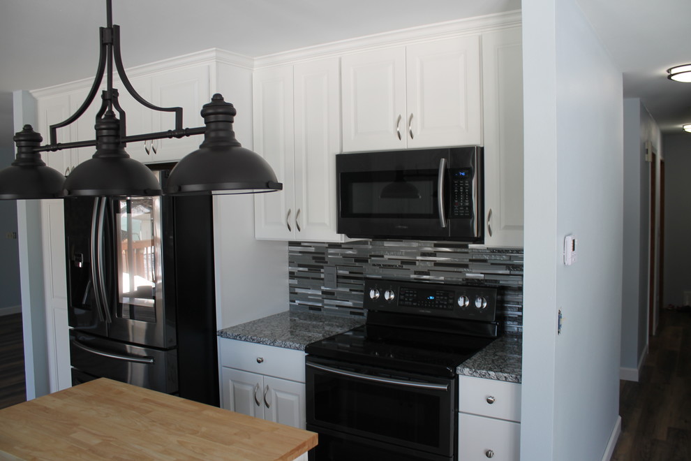 Example of a mid-sized transitional u-shaped dark wood floor and brown floor kitchen design with an undermount sink, raised-panel cabinets, white cabinets, granite countertops, multicolored backsplash, matchstick tile backsplash, stainless steel appliances and an island