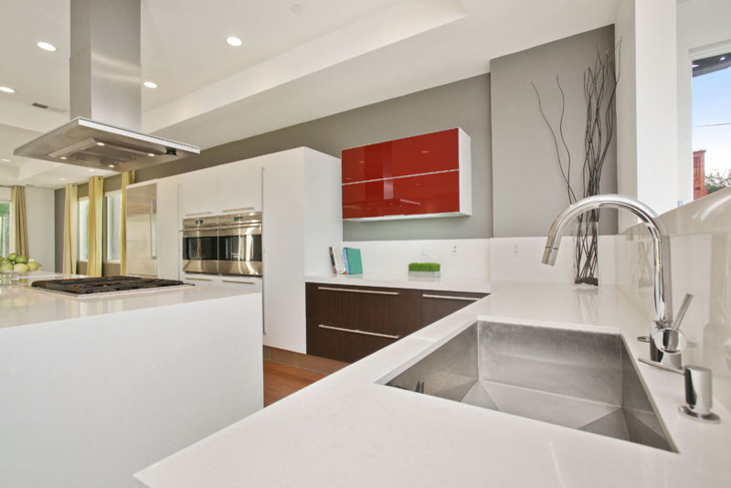 This is an example of a large contemporary galley open plan kitchen in San Francisco with an integrated sink, flat-panel cabinets, dark wood cabinets, quartz benchtops, white splashback, stainless steel appliances, light hardwood floors and with island.