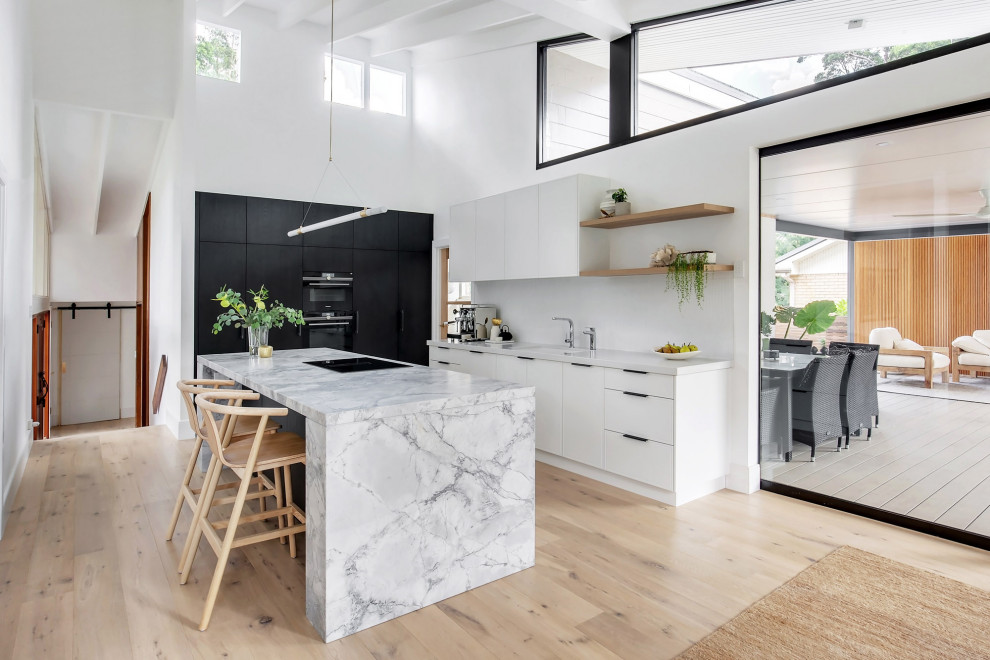 This is an example of a mid-sized modern l-shaped open plan kitchen in Sydney with an undermount sink, flat-panel cabinets, dark wood cabinets, granite benchtops, white splashback, matchstick tile splashback, black appliances, light hardwood floors, with island, beige floor, grey benchtop and exposed beam.