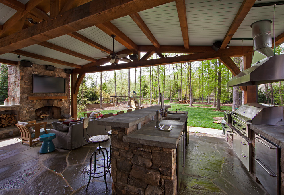 Large traditional backyard patio in Charlotte with an outdoor kitchen, natural stone pavers and a roof extension.