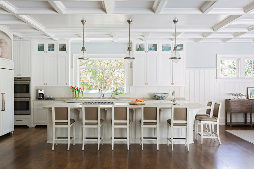 This is an example of a beach style l-shaped open plan kitchen in Charleston with recessed-panel cabinets, white cabinets, stainless steel appliances, dark hardwood floors, with island, brown floor and beige benchtop.