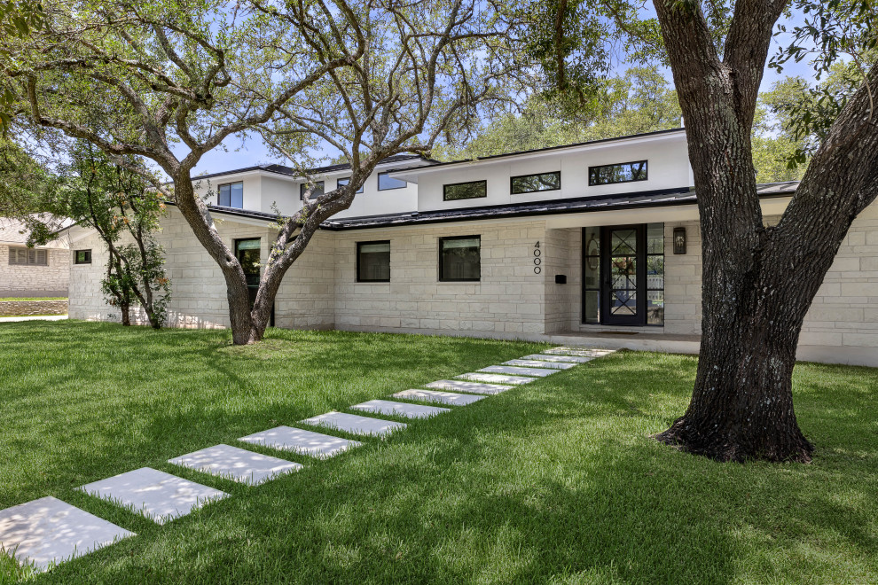 Transitional two-storey white house exterior in Austin with stone veneer, a metal roof and a black roof.