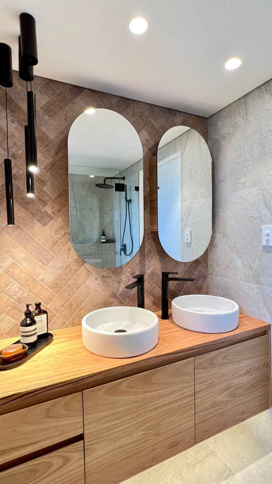 This is an example of a small mediterranean bathroom in Sydney with flat-panel cabinets, brown cabinets, a freestanding tub, a curbless shower, a wall-mount toilet, beige tile, ceramic tile, beige walls, ceramic floors, a drop-in sink, wood benchtops, beige floor, a hinged shower door, brown benchtops, a double vanity and a floating vanity.