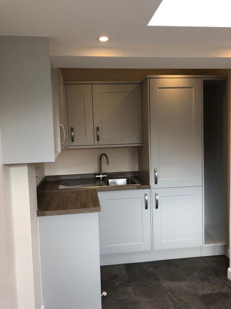 Design ideas for an expansive traditional l-shaped utility room in Hampshire with a drop-in sink, shaker cabinets, green cabinets, laminate benchtops, beige splashback, yellow walls, a side-by-side washer and dryer, brown benchtop, vaulted, timber splashback, laminate floors and grey floor.