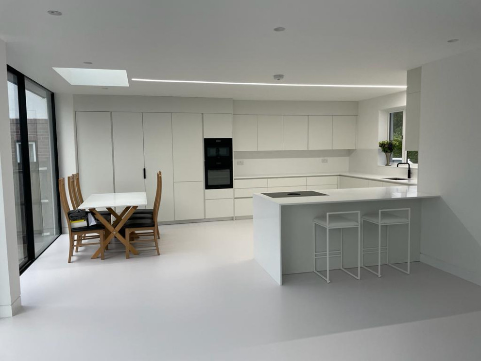 Small contemporary u-shaped open plan kitchen in London with beaded inset cabinets, white cabinets, quartzite benchtops, white splashback, black appliances, white floor, white benchtop and coffered.