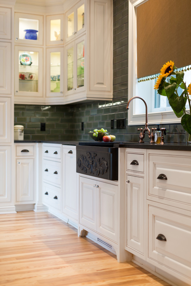 Small traditional u-shaped separate kitchen in Chicago with a farmhouse sink, beaded inset cabinets, white cabinets, granite benchtops, green splashback, subway tile splashback, stainless steel appliances, light hardwood floors, a peninsula and black benchtop.