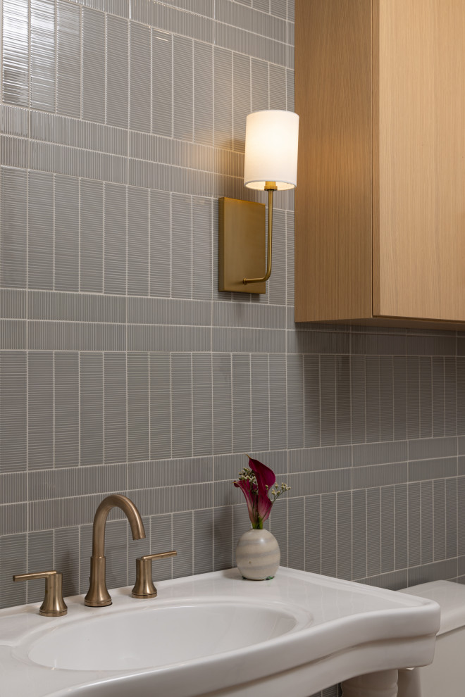 Immagine di un piccolo bagno di servizio con WC monopezzo, piastrelle grigie, piastrelle in gres porcellanato, pareti bianche, parquet chiaro, lavabo a colonna e pavimento marrone
