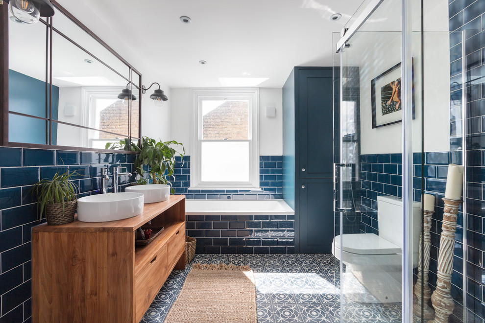 Design ideas for a mid-sized transitional kids bathroom in London with flat-panel cabinets, medium wood cabinets, a drop-in tub, a corner shower, a two-piece toilet, blue tile, subway tile, white walls, cement tiles, a vessel sink, wood benchtops, multi-coloured floor and brown benchtops.