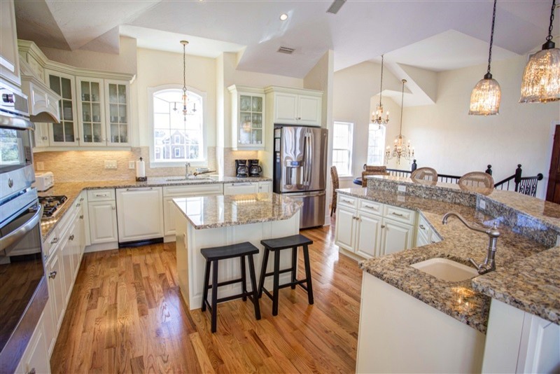 Mid-sized transitional l-shaped medium tone wood floor open concept kitchen photo with an undermount sink, raised-panel cabinets, beige cabinets, granite countertops, beige backsplash, stone tile backsplash, stainless steel appliances and an island