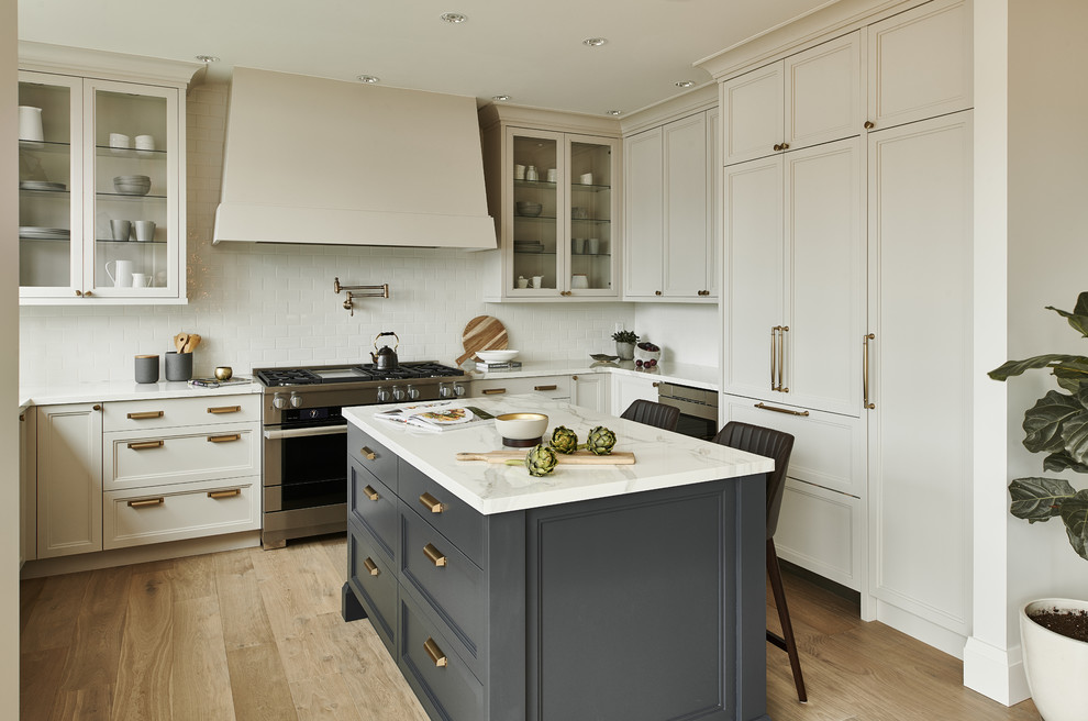 Eat-in kitchen - mid-sized transitional u-shaped light wood floor and beige floor eat-in kitchen idea in Vancouver with recessed-panel cabinets, beige cabinets, white backsplash, subway tile backsplash, an island, white countertops, a farmhouse sink, marble countertops and paneled appliances