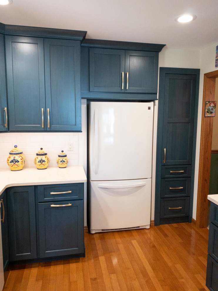 Enclosed kitchen - mid-sized transitional galley light wood floor enclosed kitchen idea with an undermount sink, flat-panel cabinets, blue cabinets, quartz countertops, white backsplash, subway tile backsplash, white appliances, a peninsula and white countertops