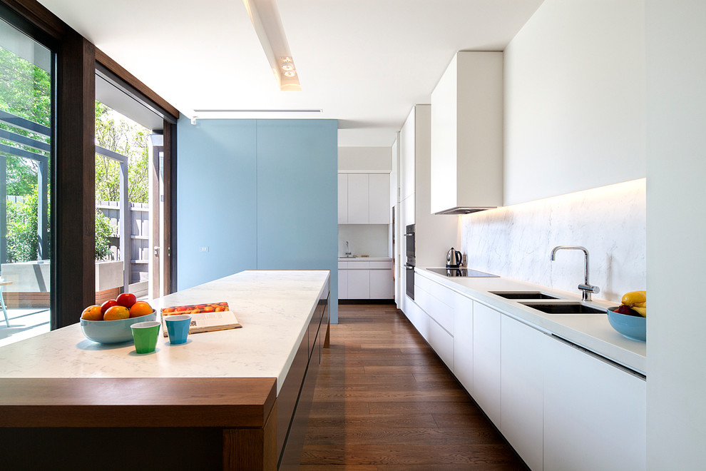 Inspiration for a mid-sized contemporary galley kitchen in Melbourne with a double-bowl sink, white cabinets, white splashback, stainless steel appliances, dark hardwood floors, with island, flat-panel cabinets and marble splashback.
