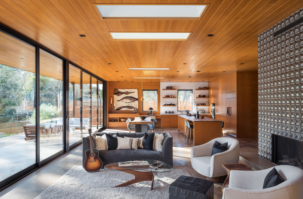 На фото: открытая гостиная комната среднего размера в стиле ретро с бетонным полом, двусторонним камином, фасадом камина из плитки, серым полом, деревянным потолком и деревянными стенами