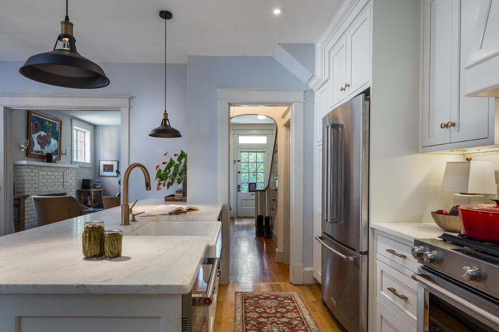 Design ideas for a mid-sized transitional galley open plan kitchen in DC Metro with a farmhouse sink, beaded inset cabinets, white cabinets, marble benchtops, white splashback, subway tile splashback, stainless steel appliances, medium hardwood floors, with island, brown floor and white benchtop.