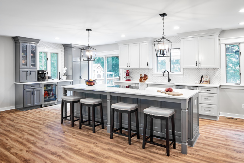 This is an example of a transitional l-shaped kitchen in Indianapolis with an undermount sink, shaker cabinets, white cabinets, white splashback, porcelain splashback, stainless steel appliances, medium hardwood floors, with island, brown floor and white benchtop.