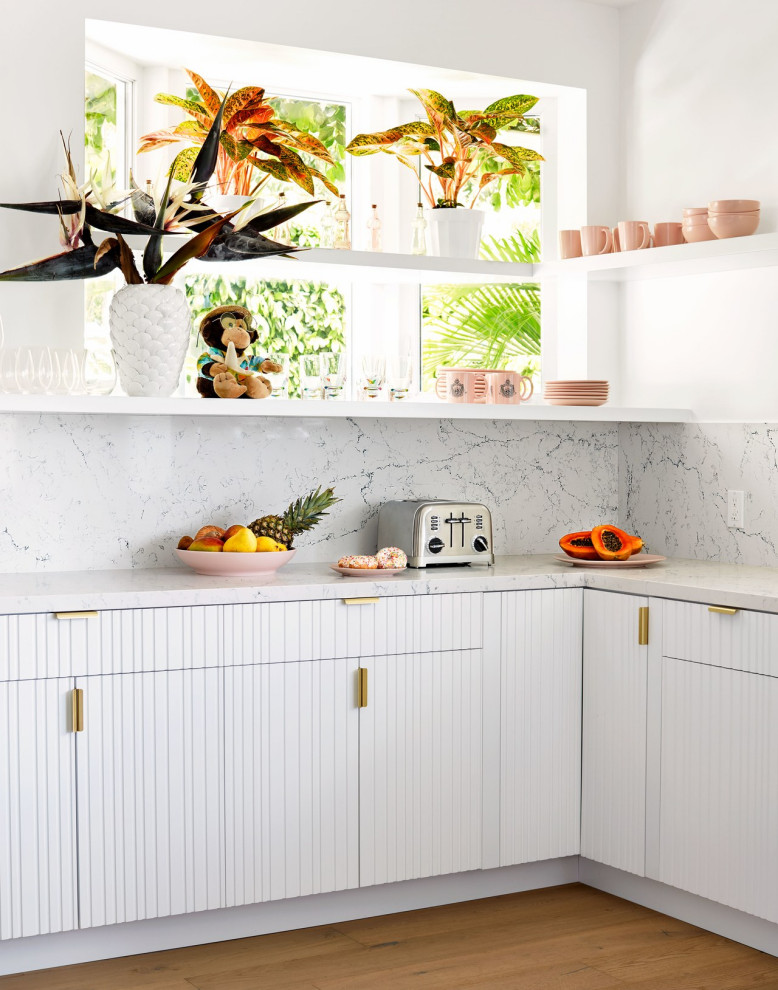 Photo of a tropical l-shaped kitchen in Los Angeles with white cabinets, white splashback, stone slab splashback, light hardwood floors, beige floor and white benchtop.