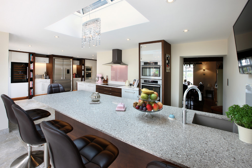 Photo of an expansive contemporary eat-in kitchen in West Midlands with a double-bowl sink, flat-panel cabinets, white cabinets, quartzite benchtops, pink splashback, glass sheet splashback, stainless steel appliances, ceramic floors, with island and grey floor.