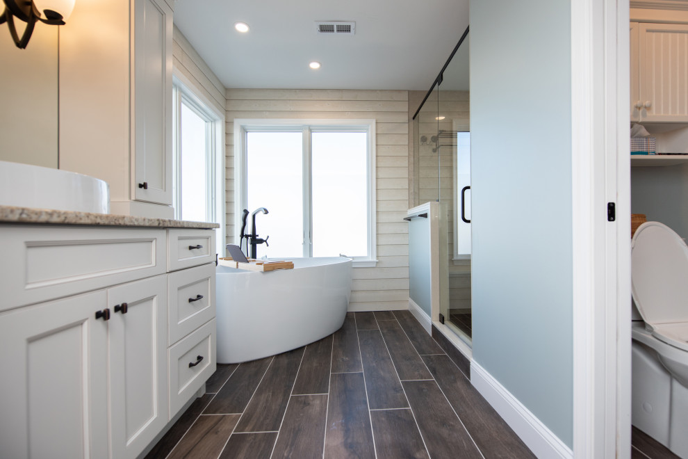 Inspiration for a medium sized nautical ensuite bathroom in Philadelphia with shaker cabinets, white cabinets, a freestanding bath, a two-piece toilet, beige tiles, porcelain tiles, white walls, porcelain flooring, a vessel sink, granite worktops, brown floors, a hinged door, multi-coloured worktops, an enclosed toilet, a single sink, a built in vanity unit and tongue and groove walls.