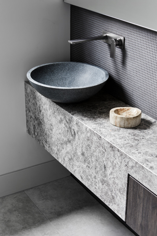 Inspiration for a small modern powder room in Melbourne with grey cabinets, a one-piece toilet, gray tile, mosaic tile, grey walls, ceramic floors, a vessel sink, limestone benchtops, grey floor, grey benchtops, a built-in vanity and flat-panel cabinets.